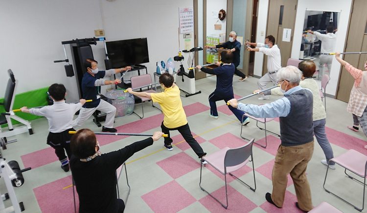 棒を使った体操で肩まわりをのばす会員